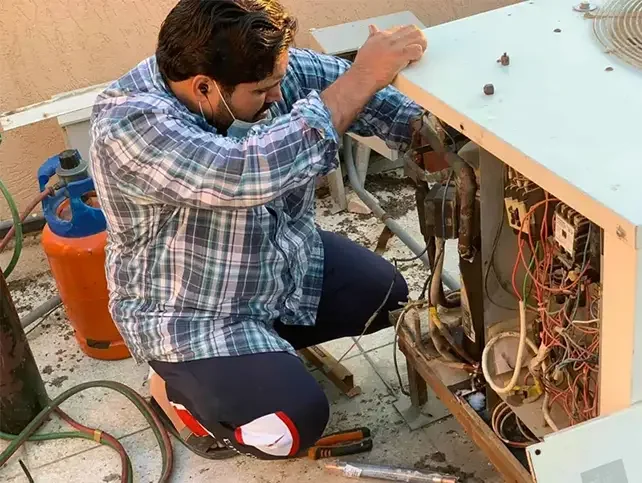 فني تكييف هندي في الكويت أثناء فحص وصيانة المكيف